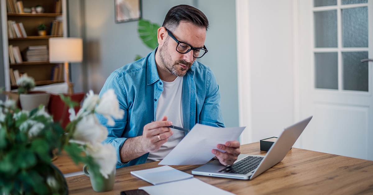 Man looks at laptop and paperwork.