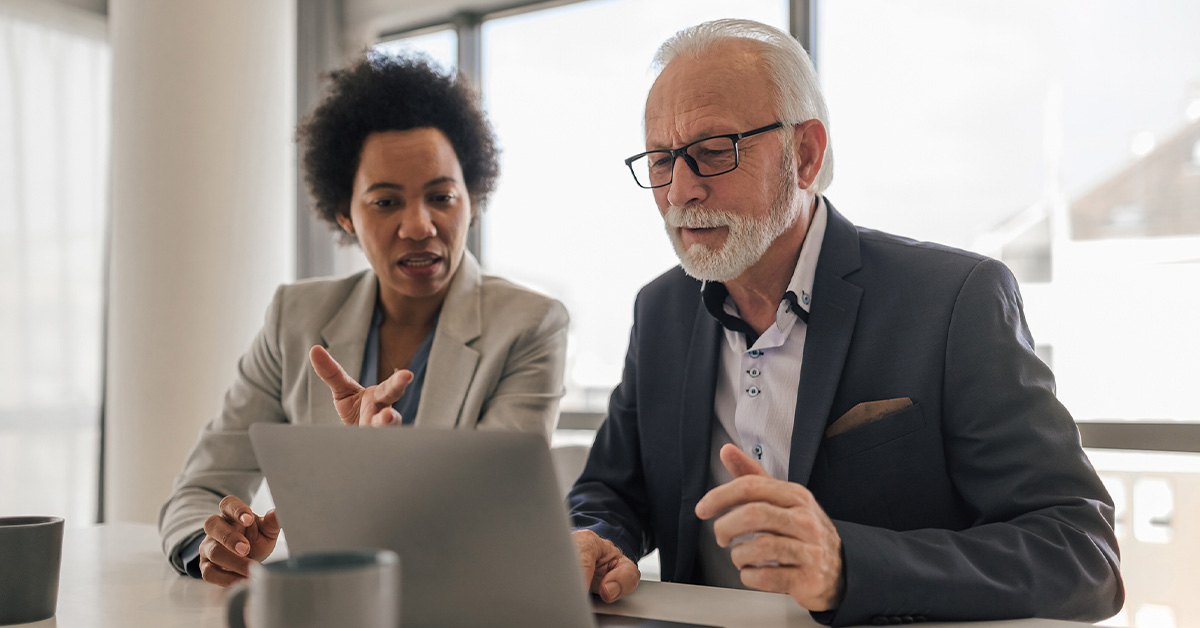 One male and one female business professional sitting at a table reviewing information on a laptop