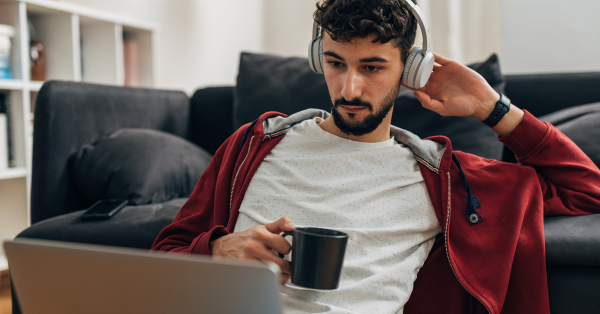 Young man wearing headphones looks at laptop screen