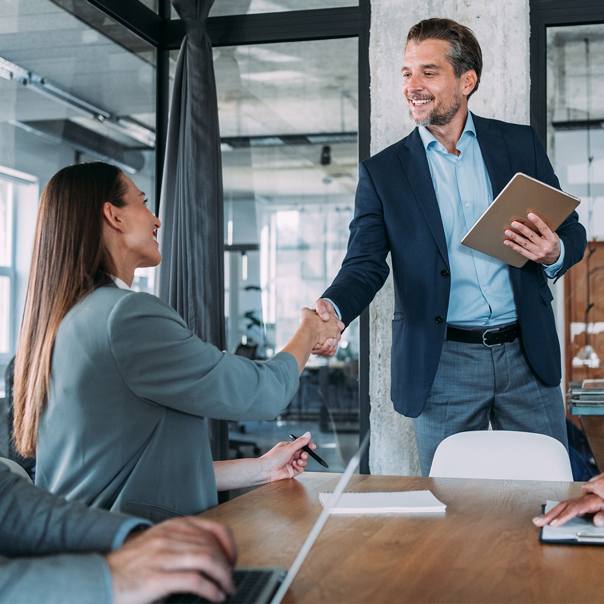 A man standing up shaking up a woman's hand in a conference room.