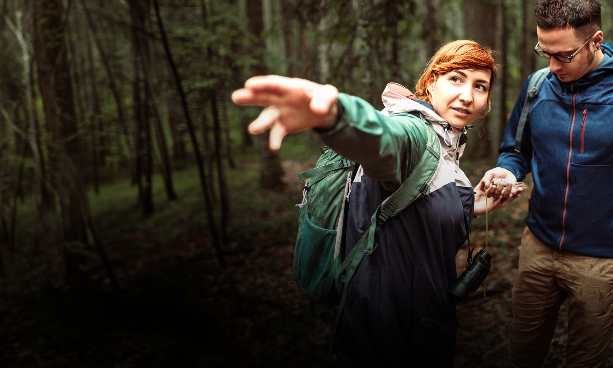 Two hikers in the woods with one holding a compass and the other pointing in a forward direction.