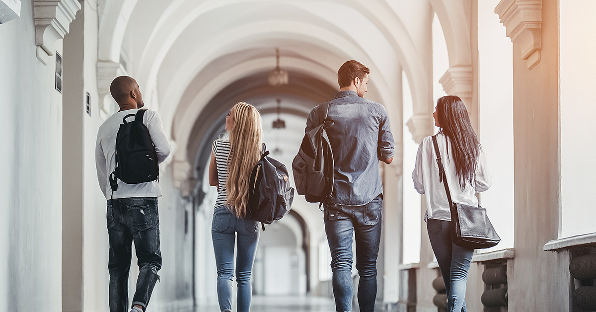 Four college students with backpacks walking down a hallway