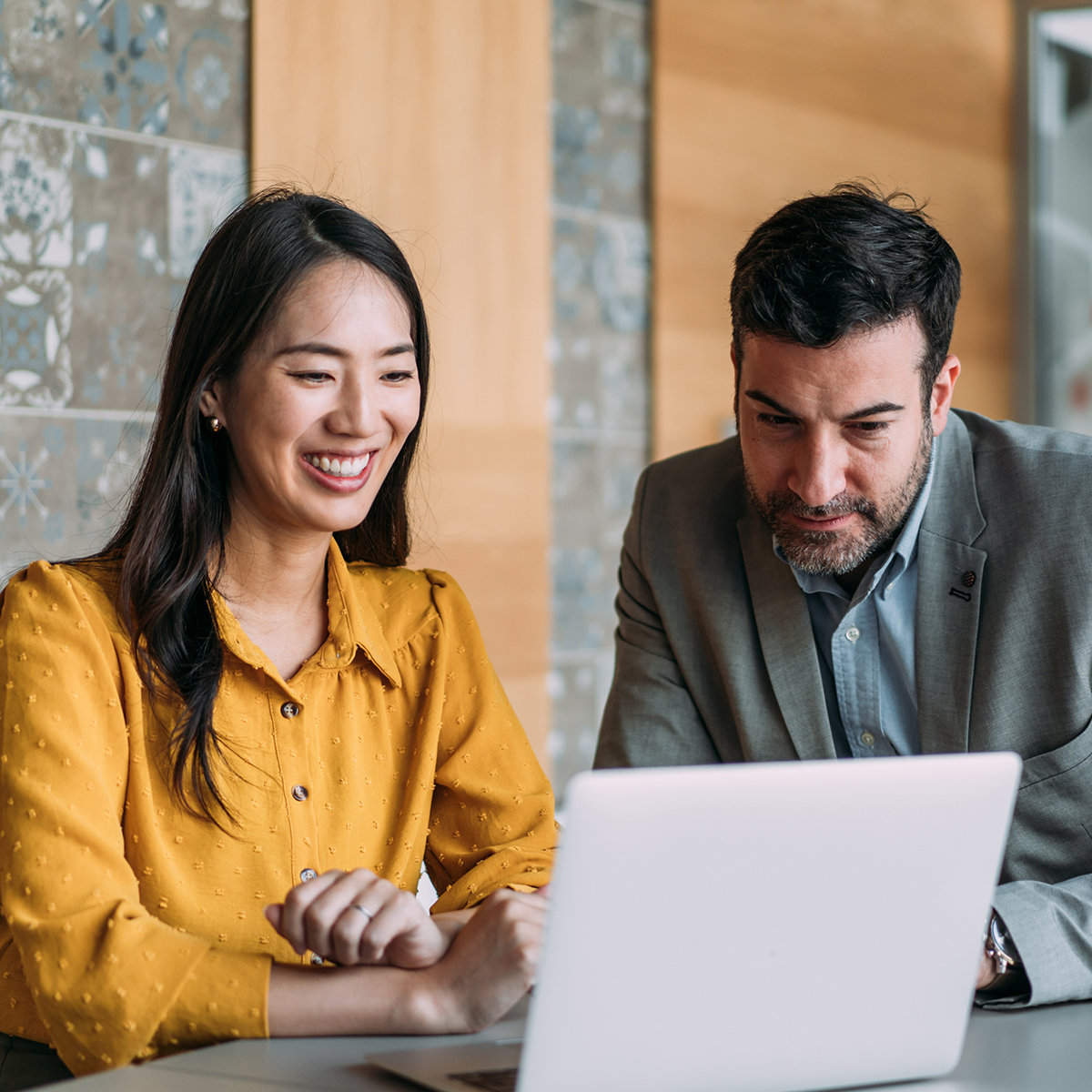 A professional couple collaborates on a business project, smiling as they work together on a laptop with internet access.