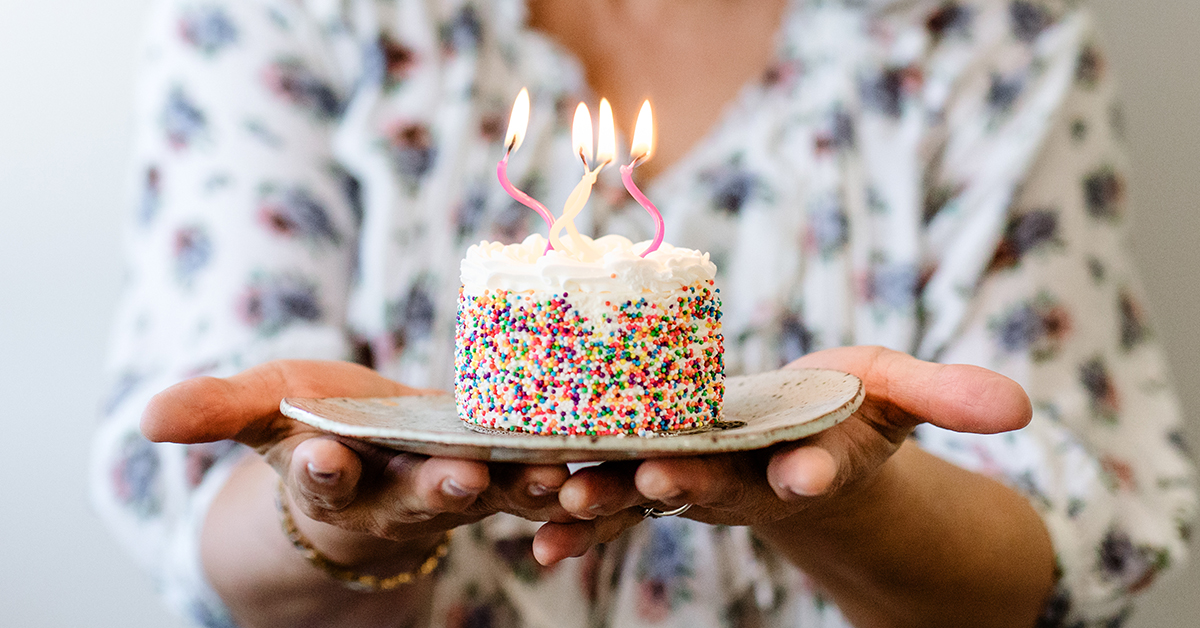 A person holding a plate out with a mini cake with candles