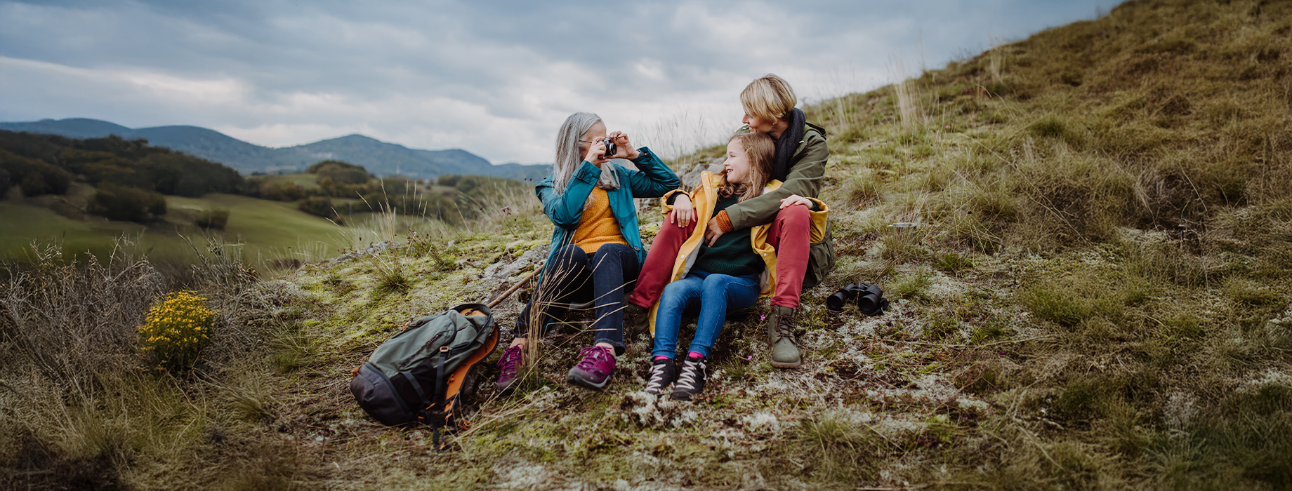 Three multigenerational women sitting on the side of hill with one taking a picture of the other two