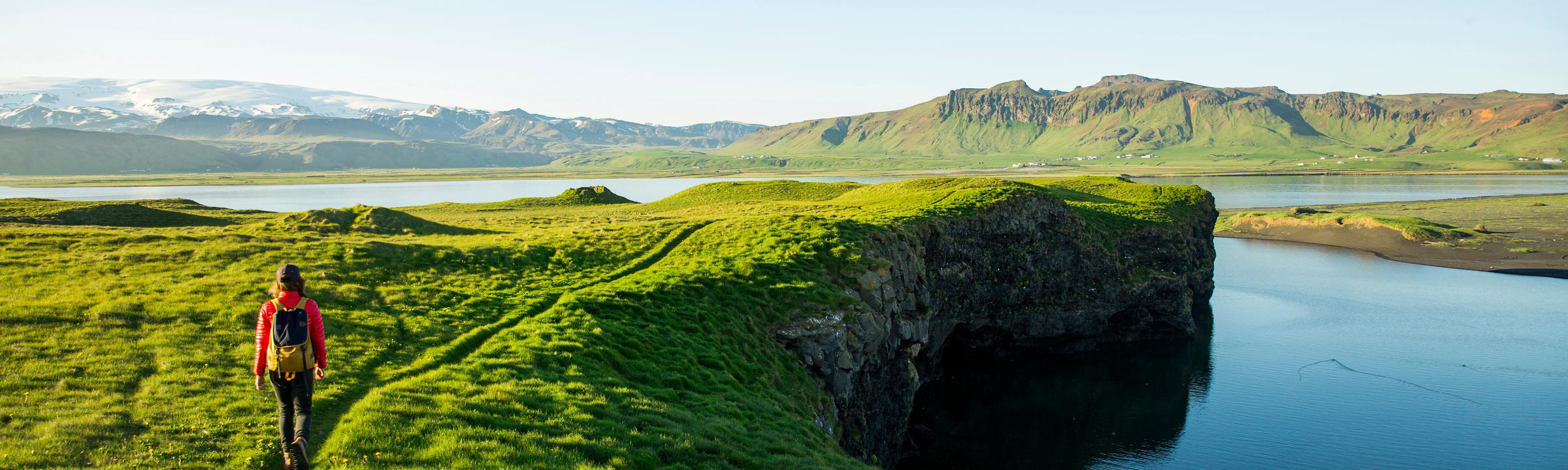 A serene landscape featuring green hills, towering mountains, and a sky filled with scattered clouds above the horizon.