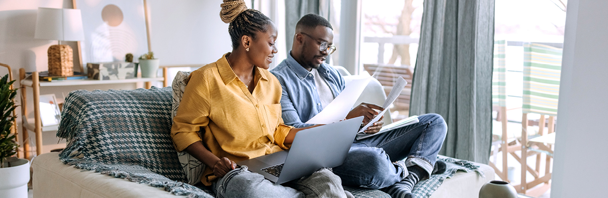 Man and woman in the living room with laptop and paperwork.