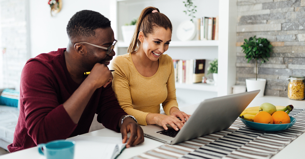 A young couple sitting at a kitchen island, looking at their laptop