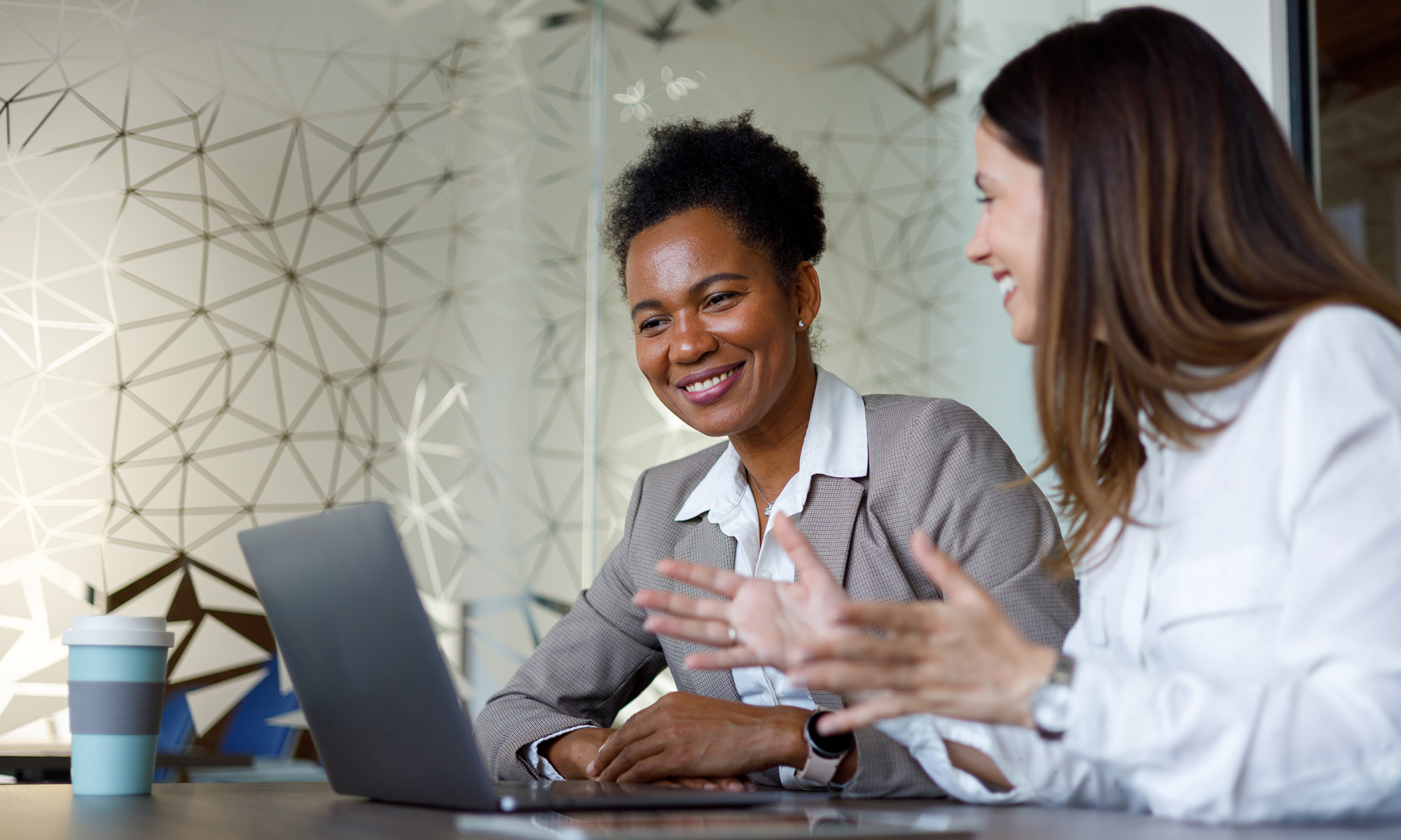 Two professionals are talking in front of a laptop.