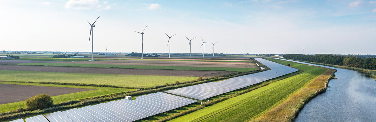 Solar panels and wind turbines stand in a green countryside, showcasing renewable energy sources in a natural setting.
