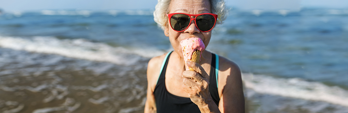  An older woman wearing sunglasses enjoys an ice cream cone on a sunny day.