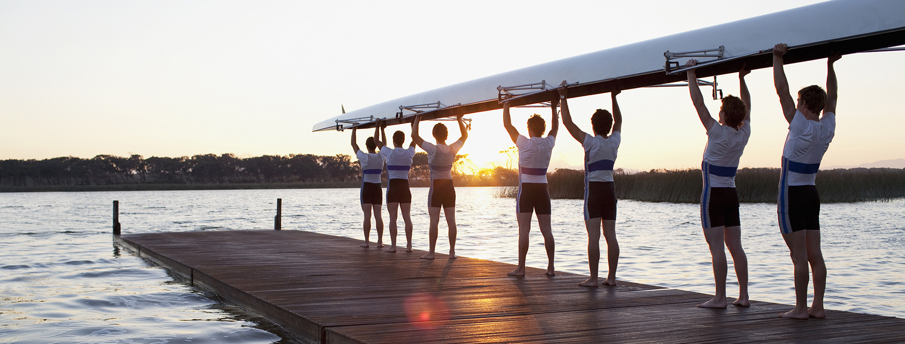 A team of rowers on a dock holding their boat over their heads