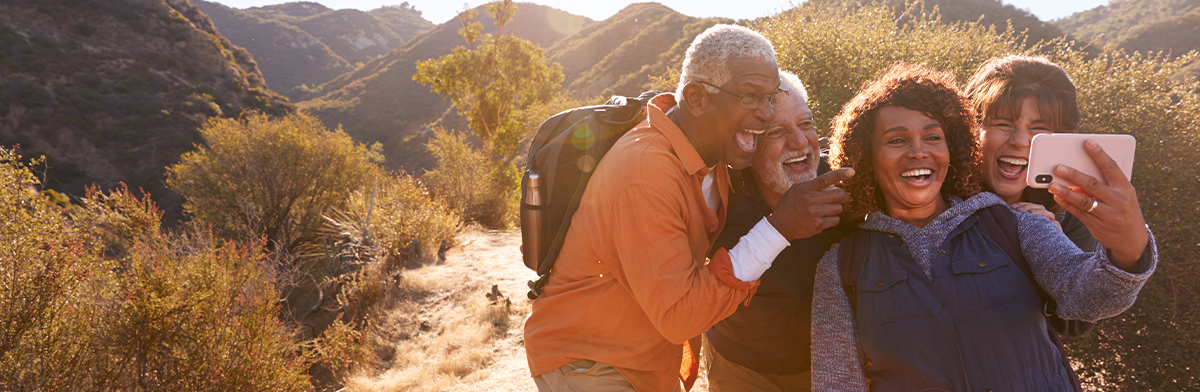 Three people smiling and taking a selfie against a scenic mountain backdrop.