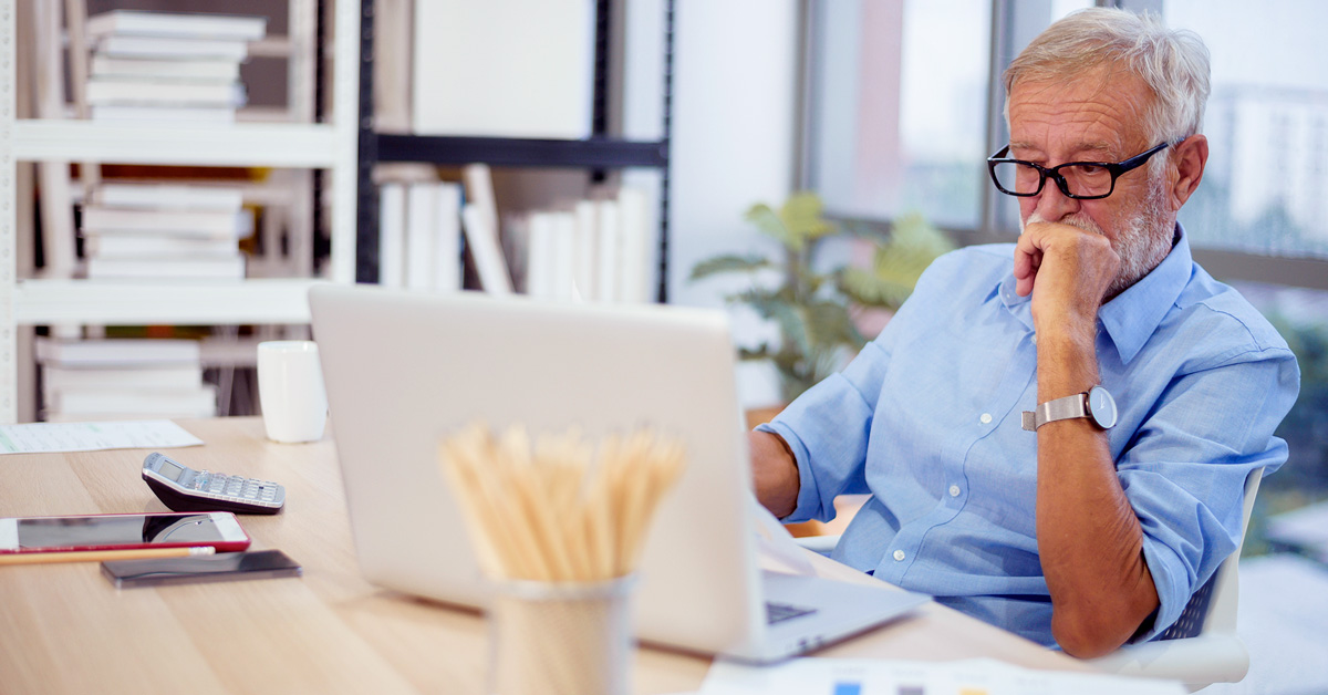Older man sitting at a table staring at his computer with a concerned look