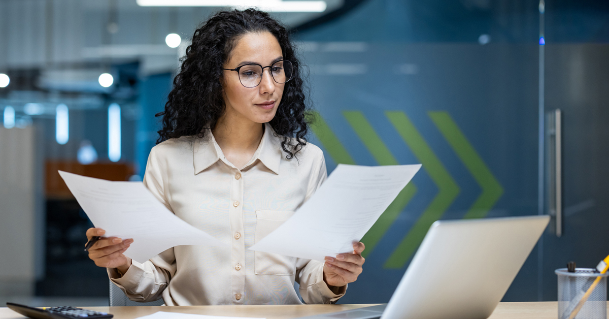 A women sitting at a desk looking at two pieces of paper.